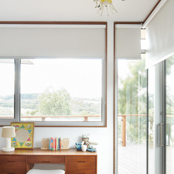 Wooden desk in front of dark white roller blinds.