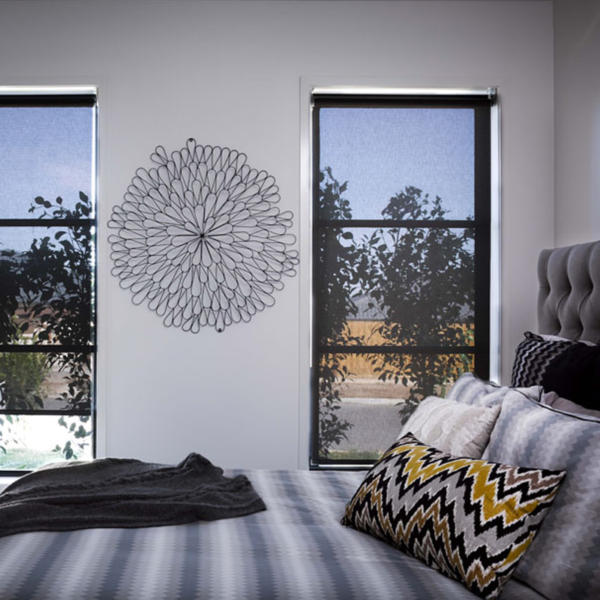 Bedroom with modern wall hanging between windows with black screen blinds.